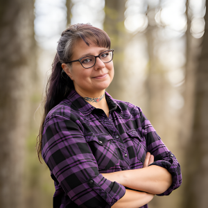 Chris Prebble, LPC, standing among trees wearing a purple and black flannel shirt, arms crossed, wearing glasses, with a slight smile and a confident stance.